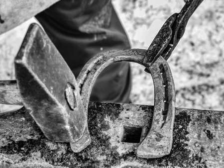 Detail of making new horseshoe in blacksmith workshop. Male farrier hammers a nail into a horseshoe. BW, Black and white,の写真素材