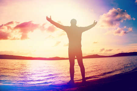 Man raising arms on sea shore. Happy man rised hands above head on beach. Abstract lighting, colorful flare.の写真素材