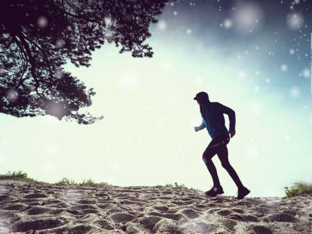 Man running at shore while snowing. Morning run against sunrise. Abstract lighting, colorful flare.の写真素材