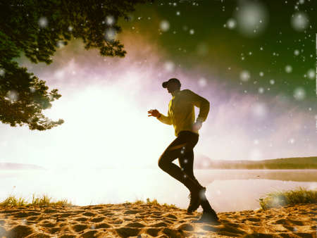 Freeze movement of running man on sandy beach at lake. Shinning snowflakes againsr low sun. Abstract lighting, colorful flare.の写真素材