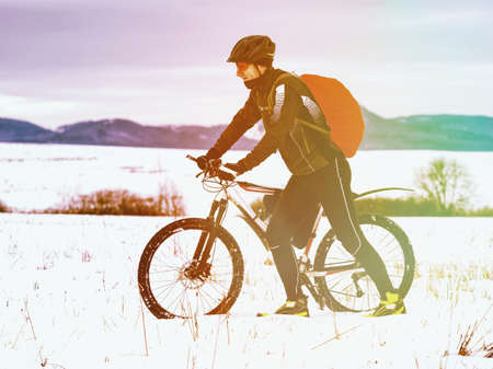 Sport cyclist pushing bike in the hardest and snowy landscape during winter. Abstract lighting, colorful flare.の写真素材