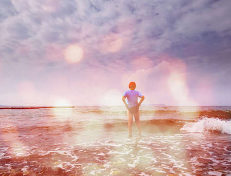 Boy stay in cold water at sea shore. Abstract lighting, colorful flare.の写真素材