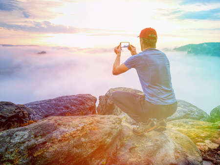 Man sit and takes phone photo of morning misty mountain valley. Hiken in outdoor wearing. Abstract lighting, colorful flare.の写真素材