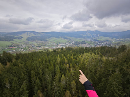 Female hand pointing into dark clouds above hilly landscape with huge forestsの写真素材