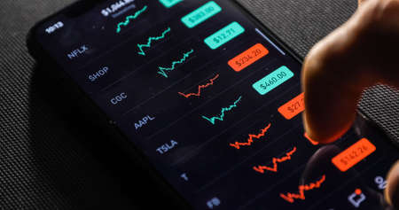 NEW YORK CITY, NY - March 23, 2020: Hand of male with smart phone checking stock market in the night room at home.のeditorial素材