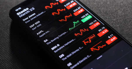 NEW YORK CITY, NY - March 23, 2020: Hand of male with smart phone checking stock market in the night room at home.のeditorial素材