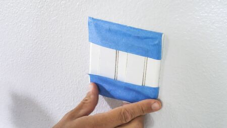 Painter Man Using Masking Blue Tape to Secure Light Switch. Preparation For Room