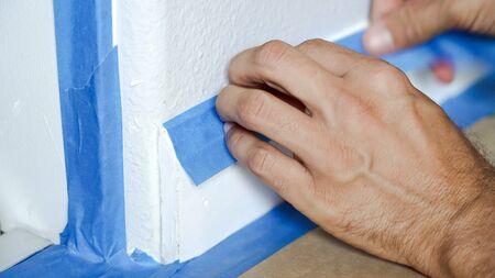 Painter Man Using Masking Blue Tape to Secure Baseboard, Moulding. Preparation For Room Painting.