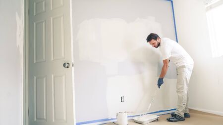 Painter man painting the wall in home, with paint roller and white color paint. Room renovations at house.の写真素材