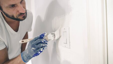 Close up of painter hands with gloves painting the wall edge with brush. A painter edging around light switch with a brush.の写真素材