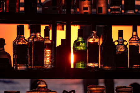 Boracay, Philippines - Jan 21, 2020: Sunset on the background of bottles standing on the bar. The sun passes through the bright glass of the bottles. Background image for the screensaver.のeditorial素材