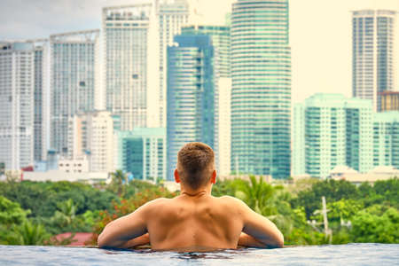 A man in the pool on the roof of the hotel. View of the city of Manila from the pool of the luxury five-star Discovery Primea hotel. Sunny weather. Skyscrapers on the background.のeditorial素材