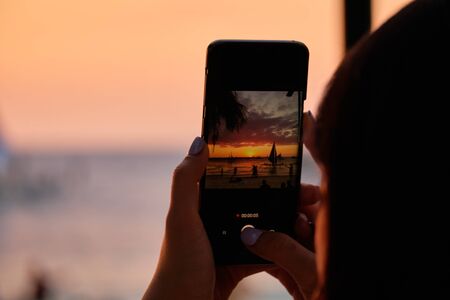 A girl takes photos of the sunset on her phone.の写真素材