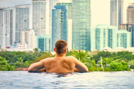 A man in the pool on the roof of the hotel. View of the city of Manila from the pool of the luxury five-star Discovery Primea hotel. Sunny weather. Skyscrapers on the background.のeditorial素材