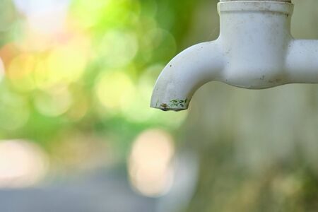 Dripping faucet in white close-up against the background of a green garden.