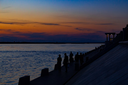 Sunset on the embankment of the Amur river in Khabarovsk. The sun set over the horizon. The embankment is lit by lanterns. People walk along the river Bank.の写真素材