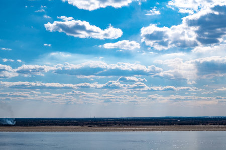 The spring Park is illuminated by the bright sun. View of a large and powerful river. On the bright blue sky beautiful white clouds.の写真素材