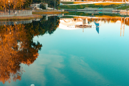 City ponds in the autumn. Trees covered with yellow and orange leaves are reflected in the water....