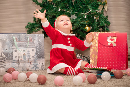 Baby girl in Santa Claus costume with gifts under the Christmas tree. Girl playing with toysの写真素材