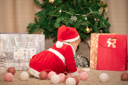 Baby girl in Santa Claus costume with gifts under the Christmas tree. Girl playing with toysの写真素材