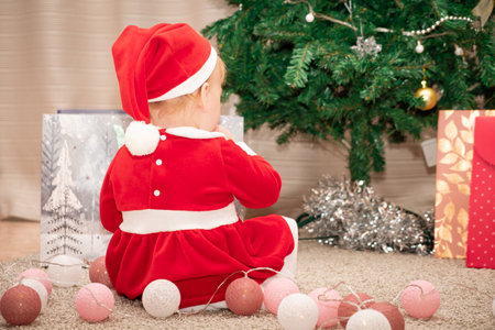 Baby girl in Santa Claus costume with gifts under the Christmas tree. Girl playing with toysの写真素材