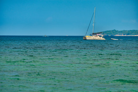 Philippines, Boracay island, Puka Beach. A white yacht is moored in the sea with a white rubber boat attached. Against the background of the mountain and palm trees of the neighboring islandの写真素材