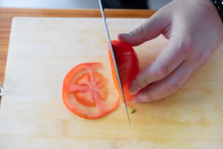 cooking, food and home concept - close up of male hand cutting tomato on cutting board at homeの写真素材