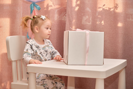 A little girl in pajamas on her birthday sits on a white chair at a childrens table, on which there is a birth.の写真素材