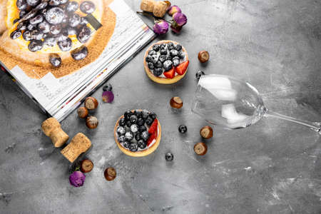 Blueberry and strawberry shortcake. There are hazelnuts, roses and wine corks on the table. Stone...