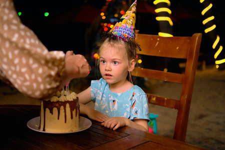 A little girl blows out the candles on her birthday cake in the evening on a tropical beachの写真素材