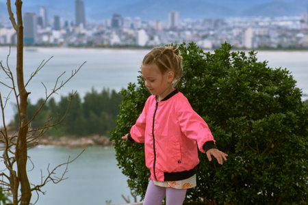 A little European girl in a pink jacket walks through the territory of the LinUng Buddhist Temple on the Seoncha Peninsula near Da Nang, Vietnamの写真素材