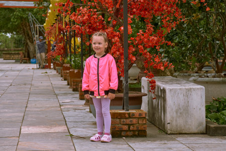 A little European girl in a pink jacket walks through the territory of the LinUng Buddhist Temple on the Seoncha Peninsula near Da Nang, Vietnamの写真素材
