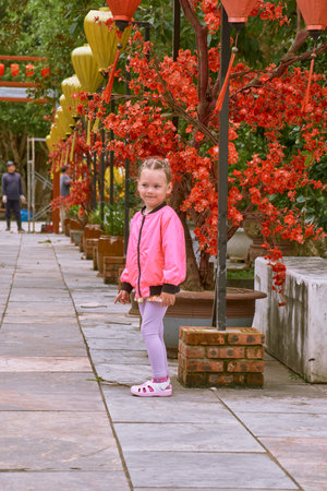 A little European girl in a pink jacket walks through the territory of the LinUng Buddhist Temple on the Seoncha Peninsula near Da Nang, Vietnamの写真素材