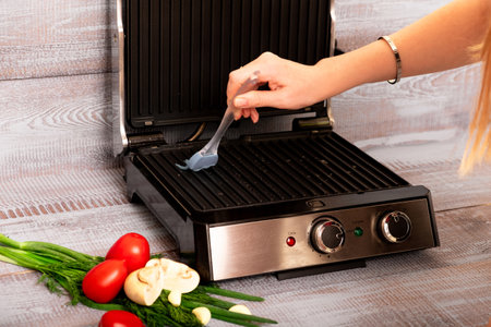 Beef is cooked on the electric grill. Around the grill vegetables laid out. On a wooden background.の写真素材