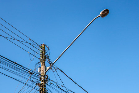 Street lamp post with emphasis on the tangle of wires and the blue sky in the backgroundの写真素材