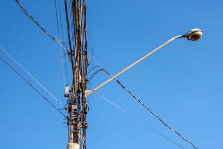 Street lamp post with emphasis on the tangle of wires and the blue sky in the background