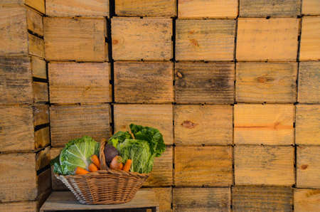 Basket with various types of vegetables and rustic wooden boxes at the bottom used for transporting natural foodsの写真素材