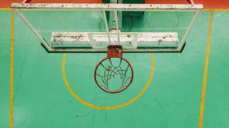 Rusty and weather-spotted basketball hoop seen from above, the green court in the background and the...
