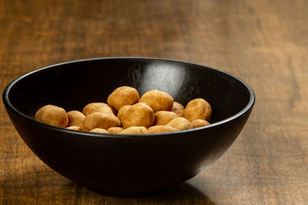 Peanut snack in a black bowl and a shiny rustic wooden table