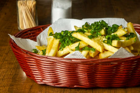 Brown wicker basket with french fries, lightly melted grated cheese and chives on top.