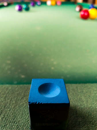 Green pool table with some balls in the background and blue chalk in the foreground.