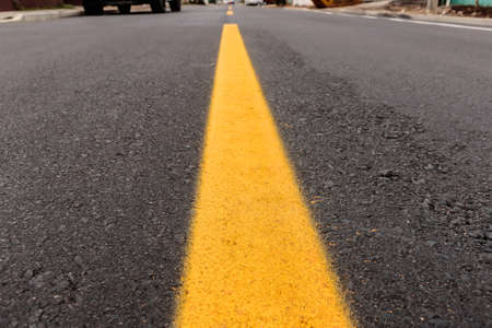 Asphalt track just made with some dirt and its texture, with a yellow stripe painted in the center of the imageの写真素材