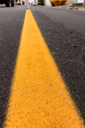 Asphalt track just made with some dirt and its texture, with a yellow stripe painted in the center of the imageの写真素材