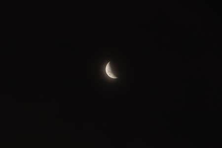 The moon in its waning phase, almost in its half, in the center of the image, shrouded in blackの写真素材