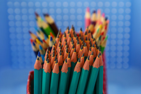 Several graphite pencils with the material in greenish tones in the foreground, in the background pencils with different colors and in the background a box with holes in blue colorの写真素材