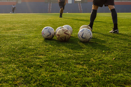 Balls on a soccer field on green grass, with players' feet, no one identified, with hard light and...