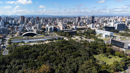 Drone on a sunny day overlooking the Oscar Niermeyer Museum, in Curitiba, with the city in the background and trees from Bosque do Papa at the bottom of the image.の写真素材