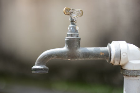 Water tap with the focus on its spout and the rest blurred. The photo has neutral colors and no water comes out of the hole.の写真素材