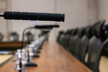 Black microphone in the foreground, in the blurred background are several other microphones and chairs in a linear plenary.の写真素材