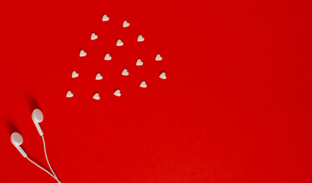 A pair of white headphones against vibrant red background with little cute white hearts. Flat layout.の写真素材